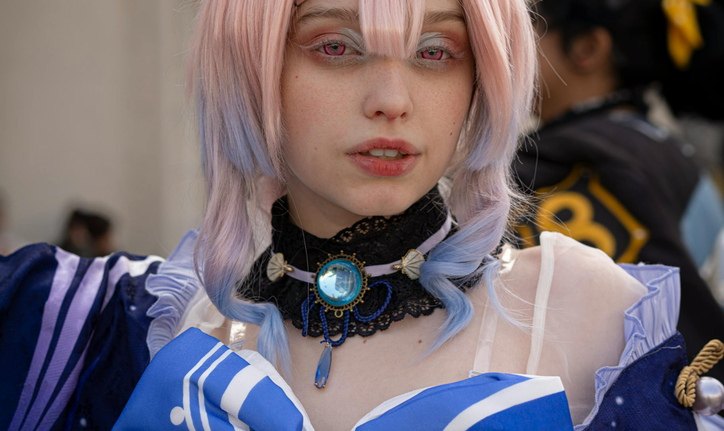 Cosplayer in detailed blue and white costume with pink wig at a convention