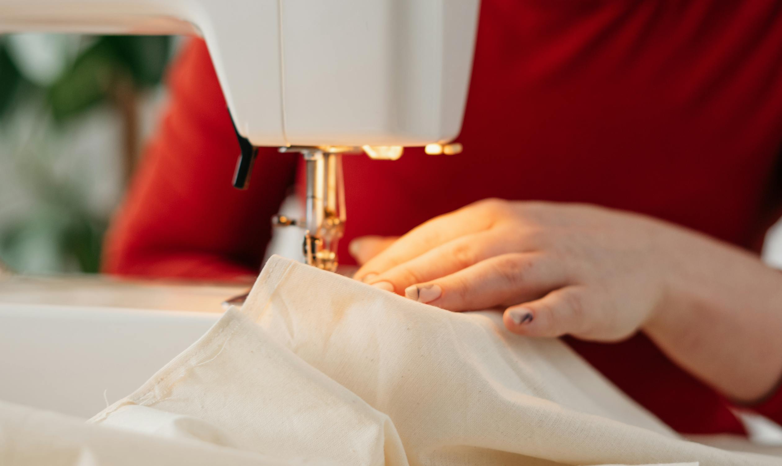 Hands guiding fabric through a sewing machine while crafting a costume