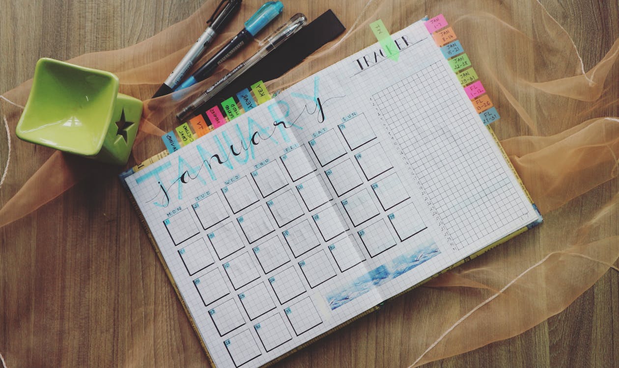 Hand-drawn bullet journal calendar with colorful tabs and pens for project planning