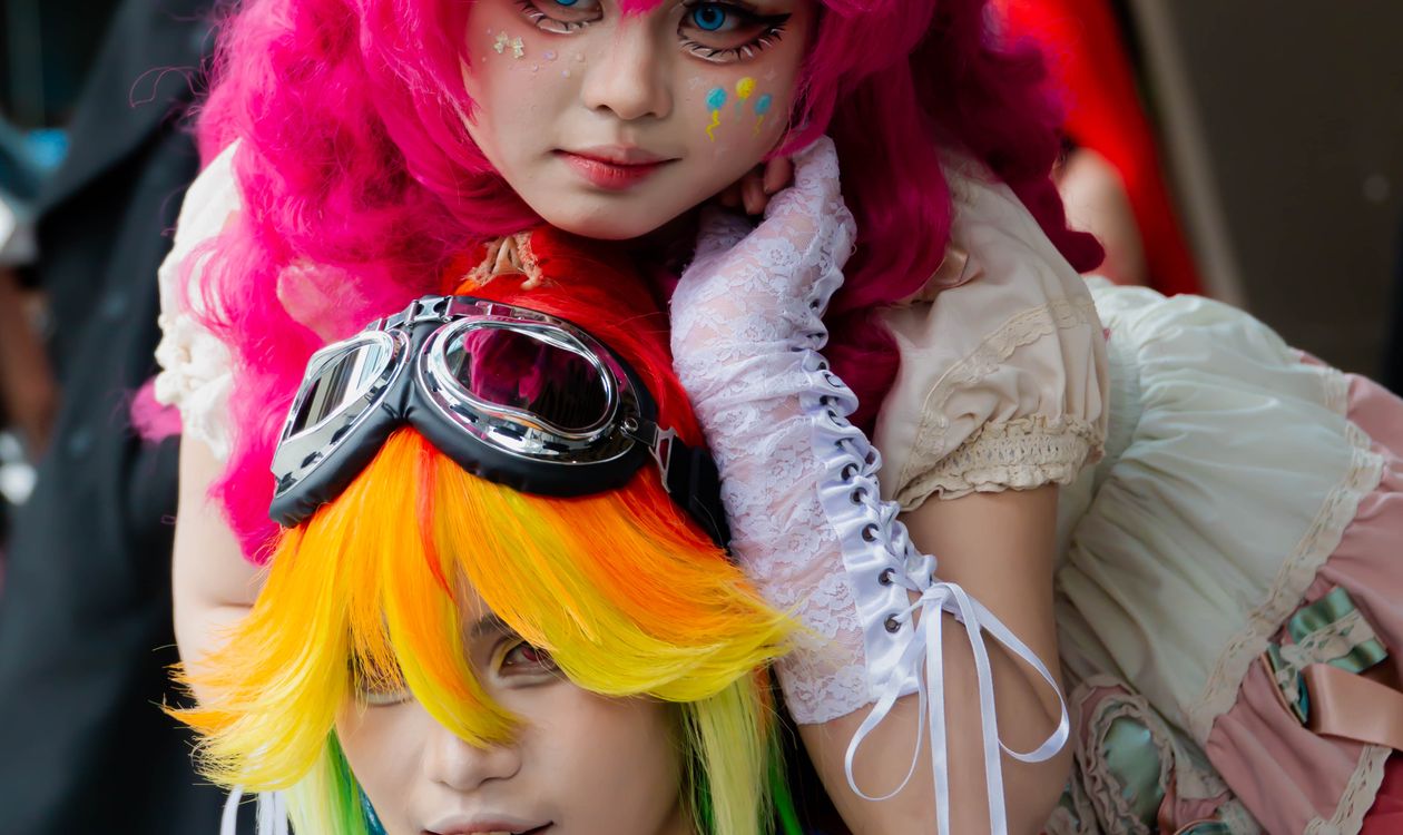Two cosplayers in colorful wigs posing closely together at an anime convention